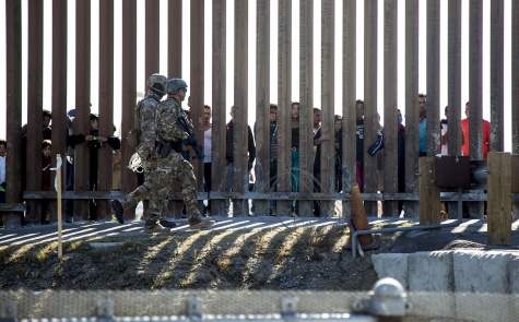 Dos soldados estadounidenses caminan desinteresados frente a un grupo de migrantes centroamericanos que miran detrás del muro fronterizo de Tijuana, el domingo 25 de noviembre Rafael Ríos